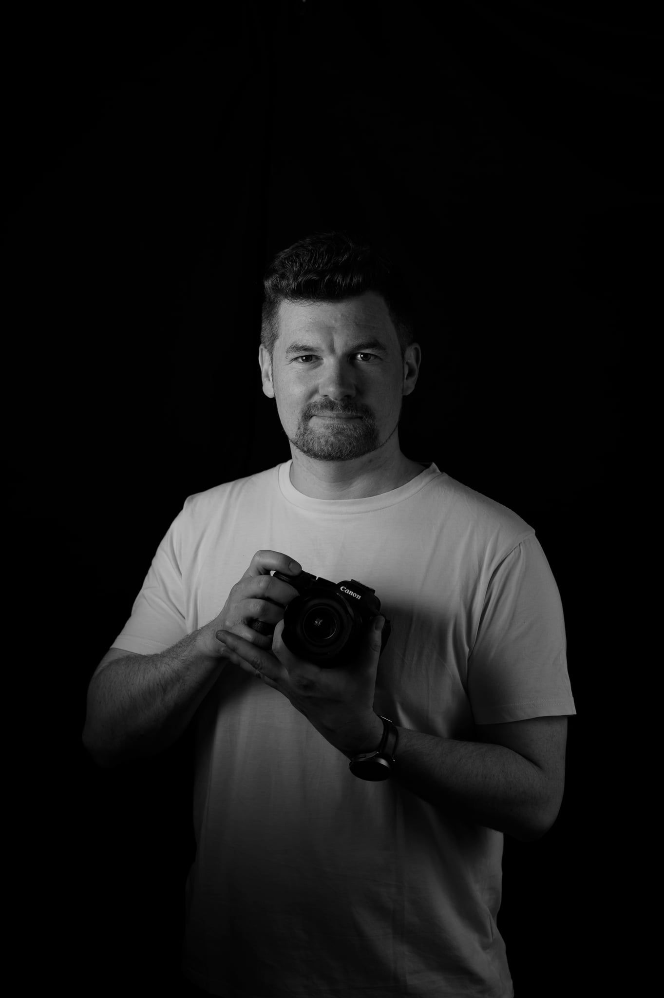 Daniel hält eine schwarze Kamera vor sein weißes T-Shirt