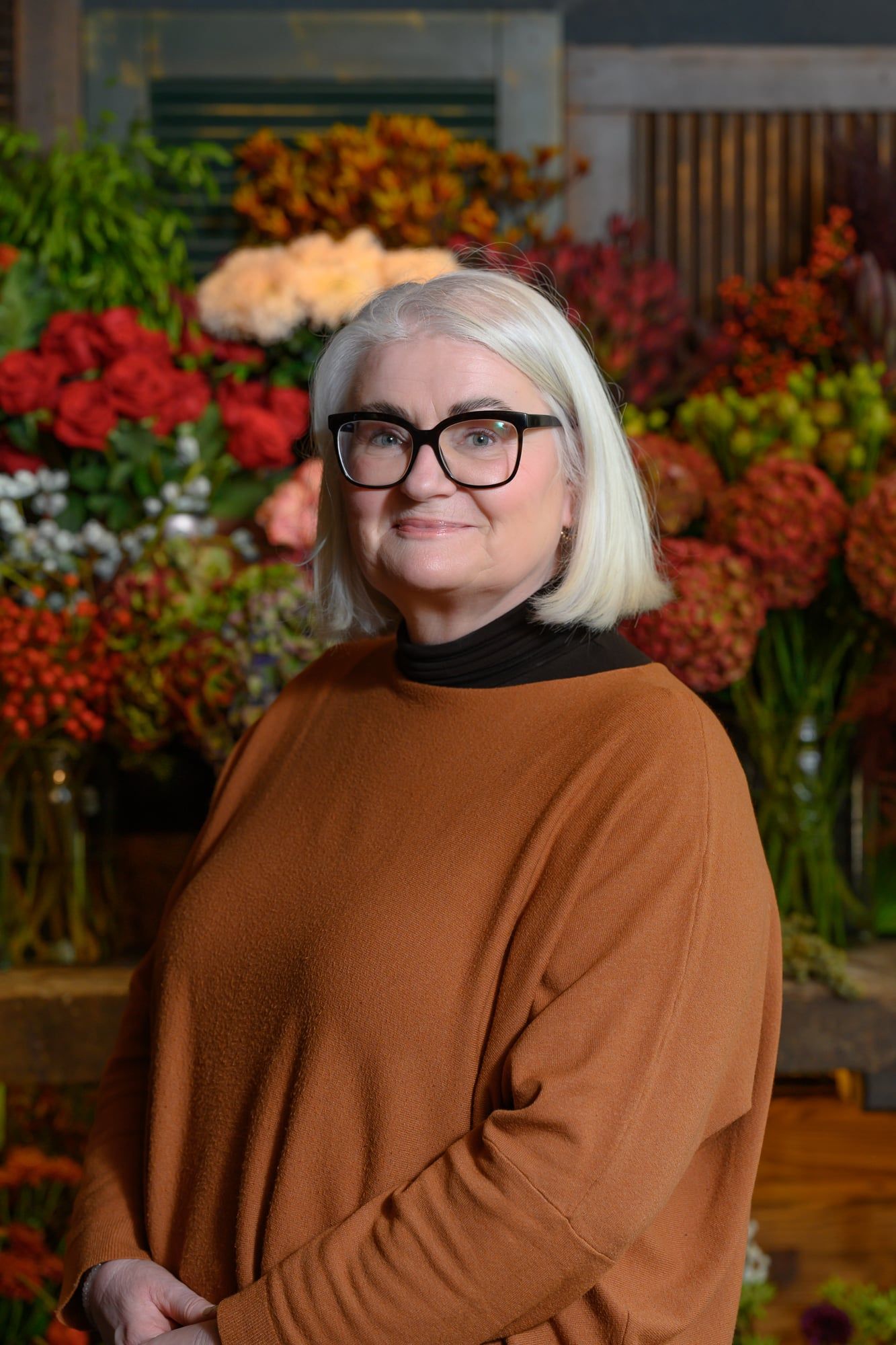 Mitarbeiterin mit grauem Haar und Brille vor bunten Blumen im Blumenladen Blickfang