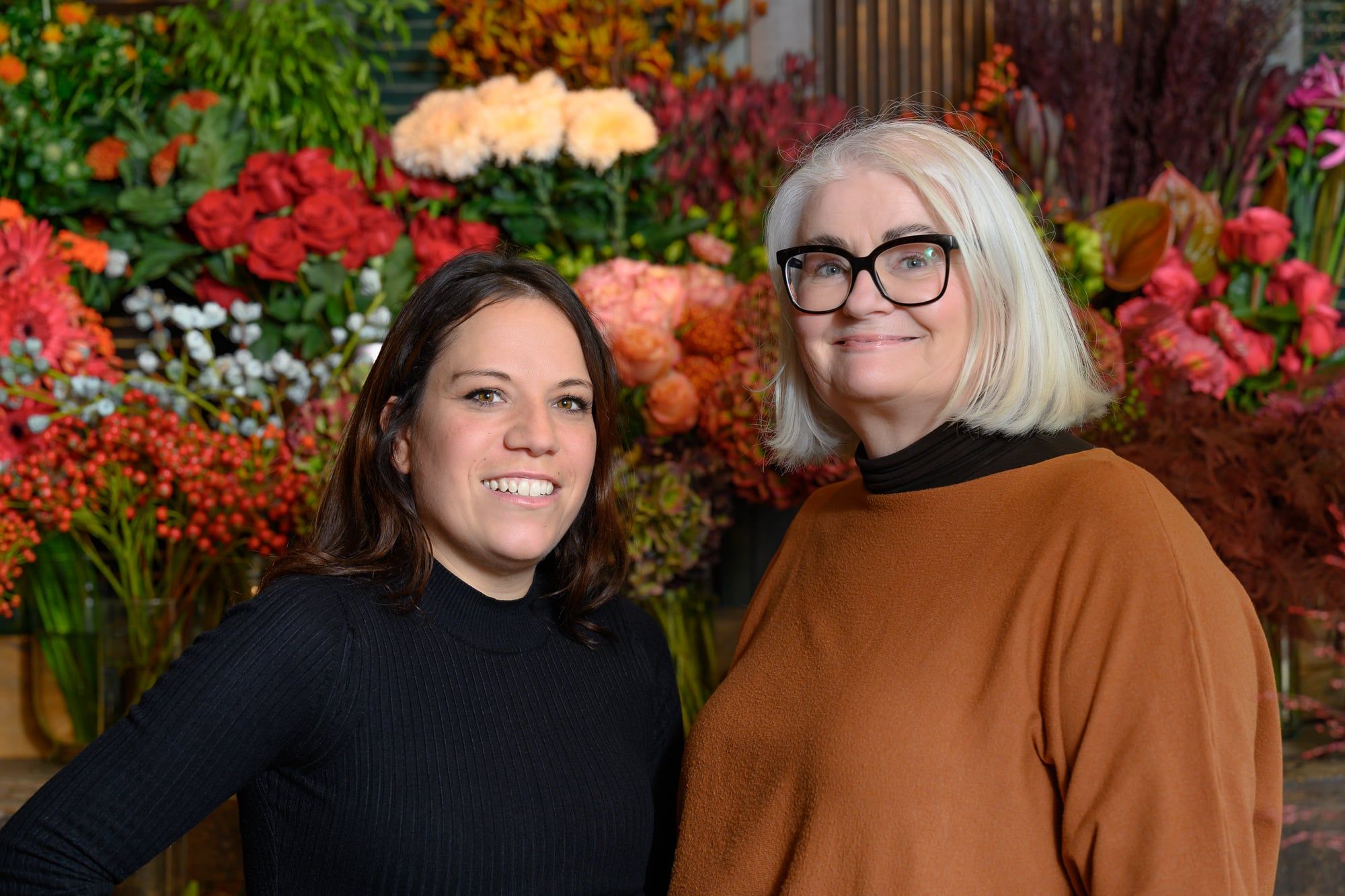 Zwei Mitarbeiterinnen des Blumenladens Blickfang in Dasing lächeln vor einer Wand voller Blumen