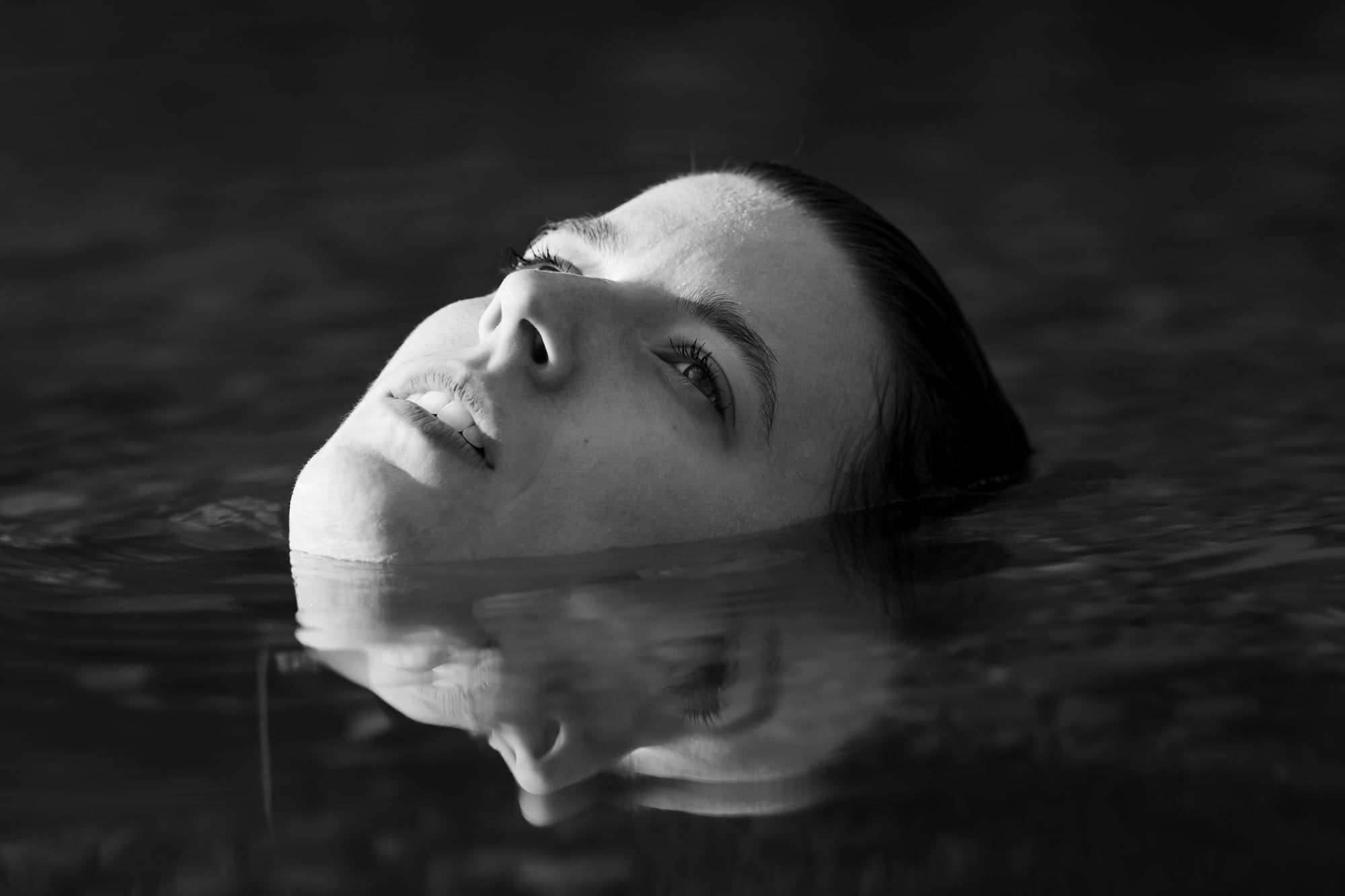 Frau liegt im dunklen Wasser, nur ihr Gesicht ragt heraus, Schwarzweiß – Portrait in Augsburg
