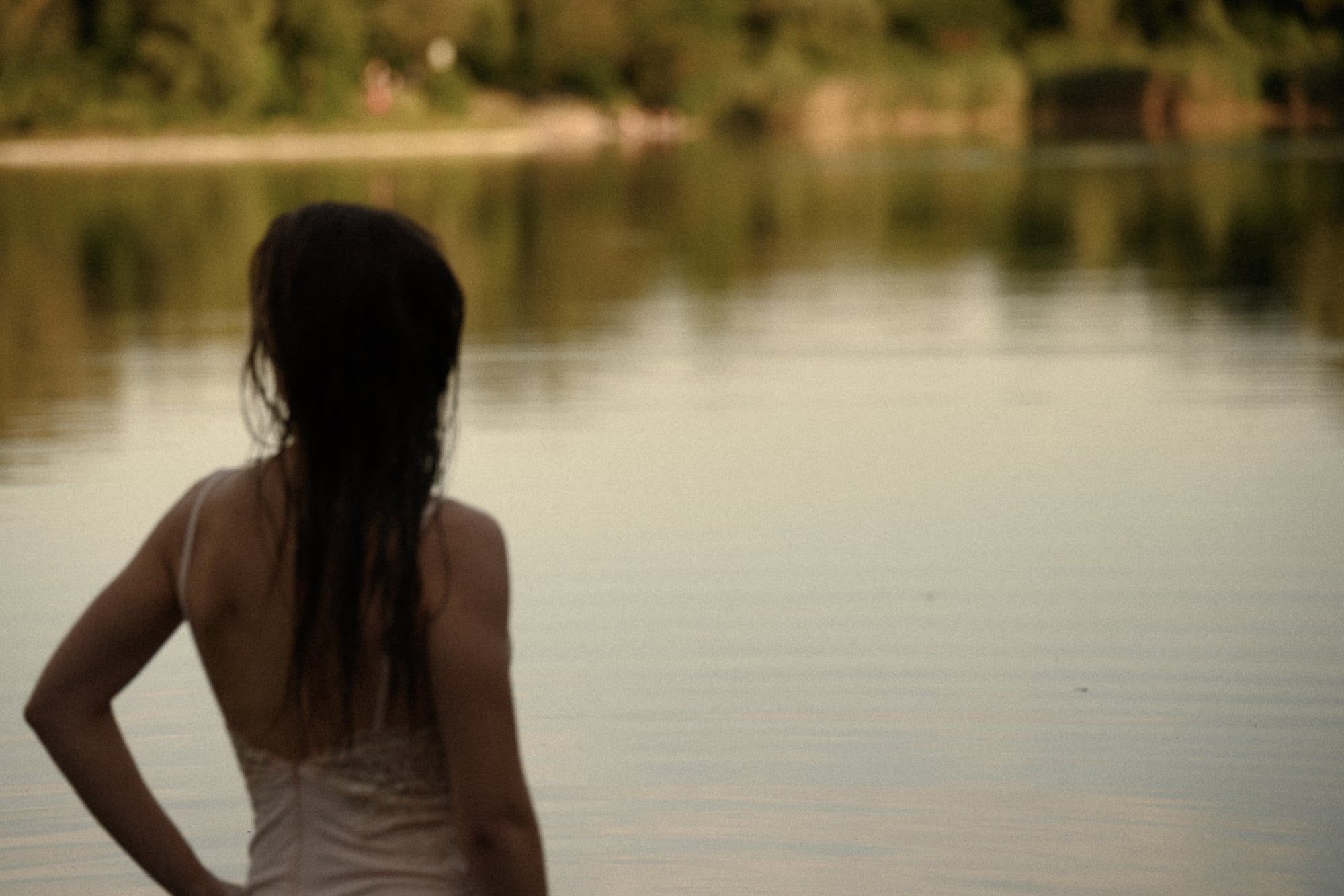 Frau steht mit dem Rücken zur Kamera an einem See im Abendlicht – Portrait in Augsburg