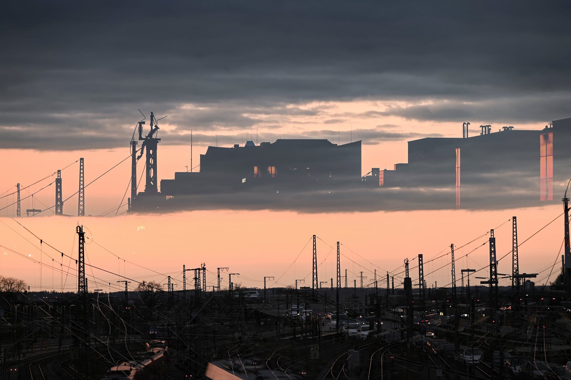 Mehrfachbelichtung: die Silhouette der Stadt schwebt in den Wolken über dem Augsburger Hauptbahnhof bei Sonnenuntergang