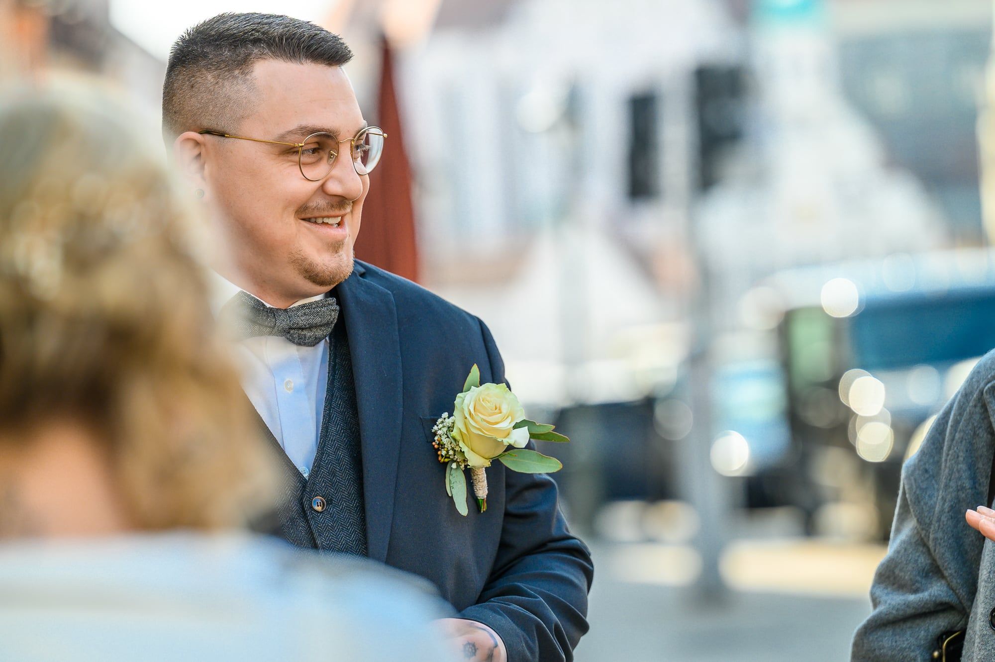 Lächelnder Bräutigam mit Brille und Anstecker im Gespräch mit Gästen – Hochzeit in Augsburg