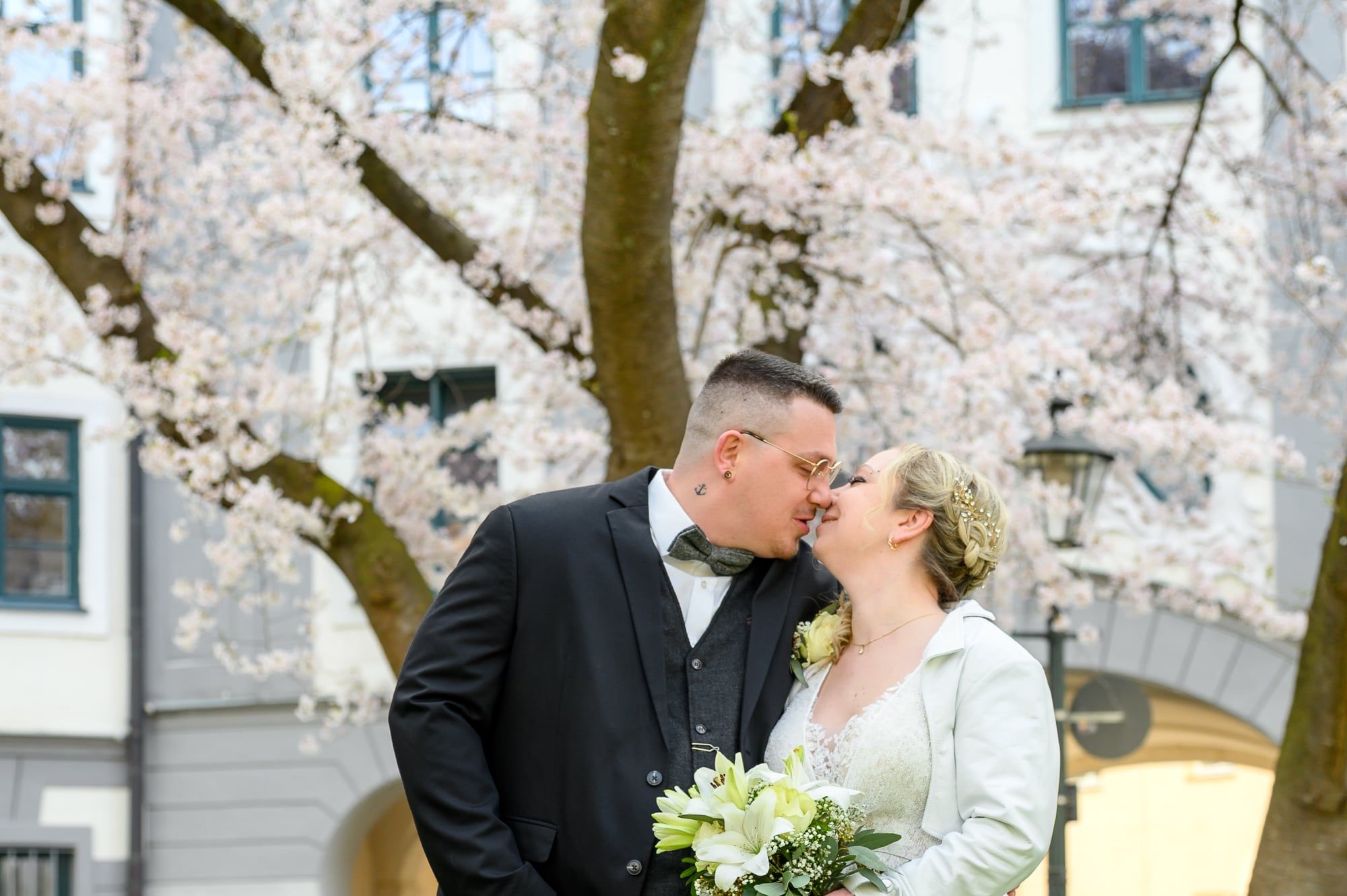 Brautpaar küsst sich unter einem blühenden Kirschbaum vor einem Altbau – Hochzeit in Augsburg