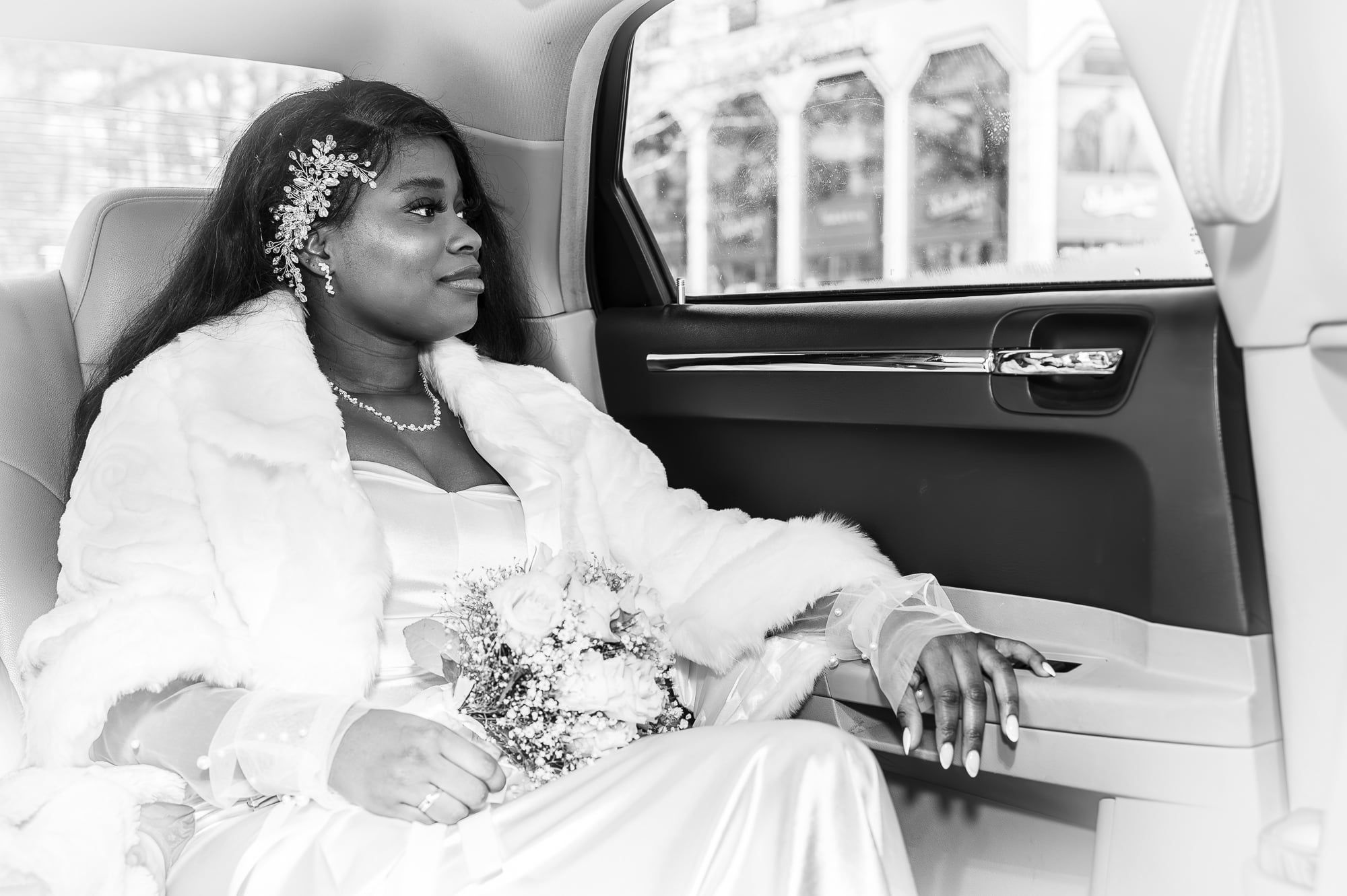 Braut mit Haarschmuck sitzt im Hochzeitsauto und blickt aus dem Fenster, Schwarzweiß – Hochzeit in Augsburg