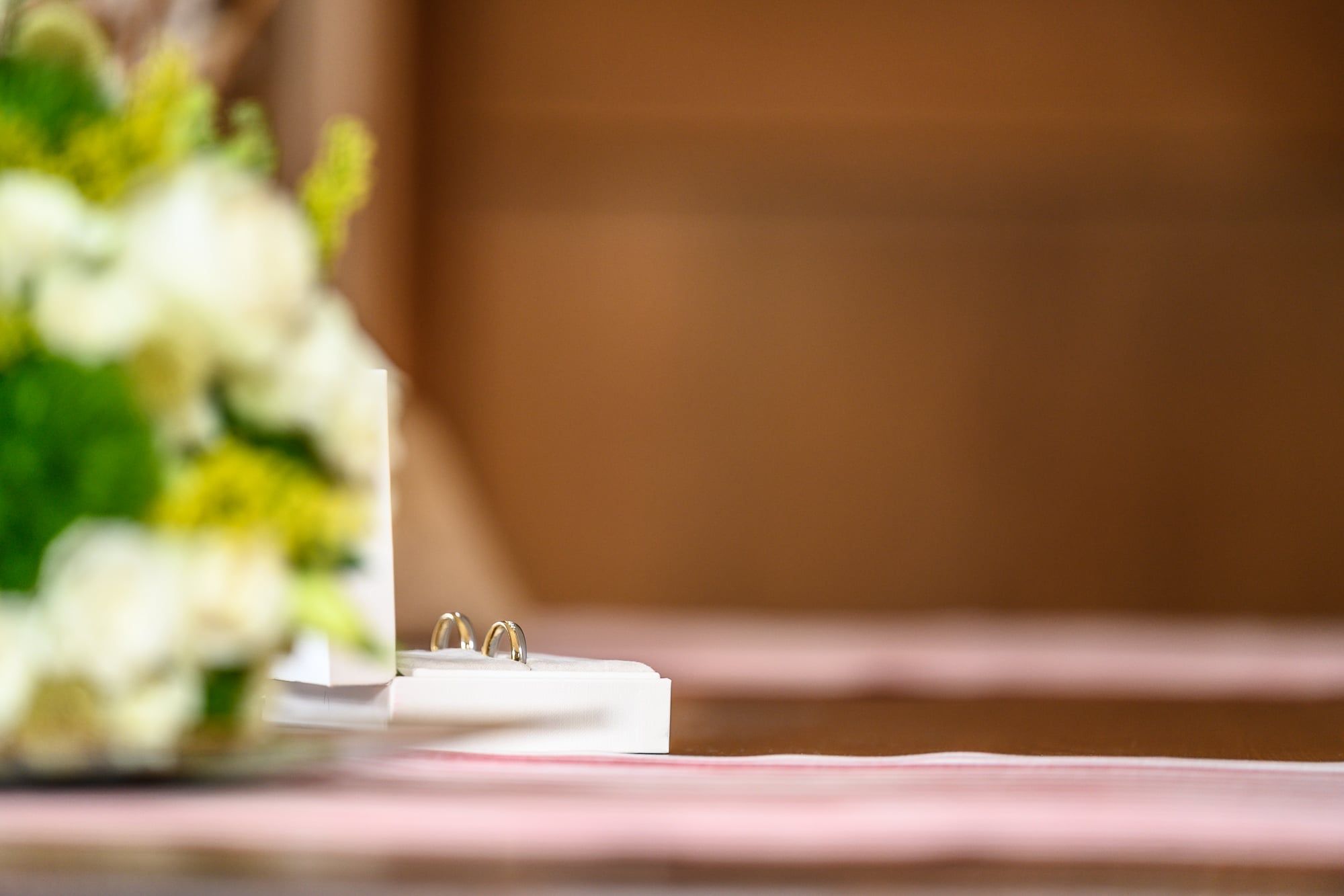 Eheringe liegen auf einem Tisch, im Vordergrund unscharfe weiße Blumen – Hochzeit in Friedberg
