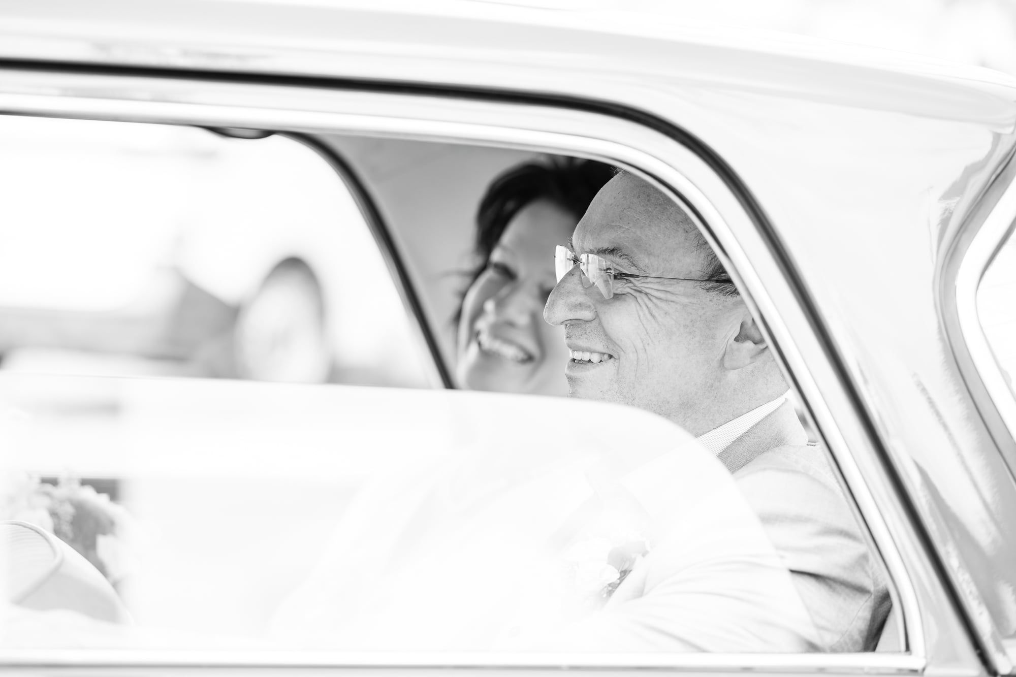 Brautpaar lacht im Fond eines Oldtimers, Schwarzweiß – Hochzeit in Friedberg