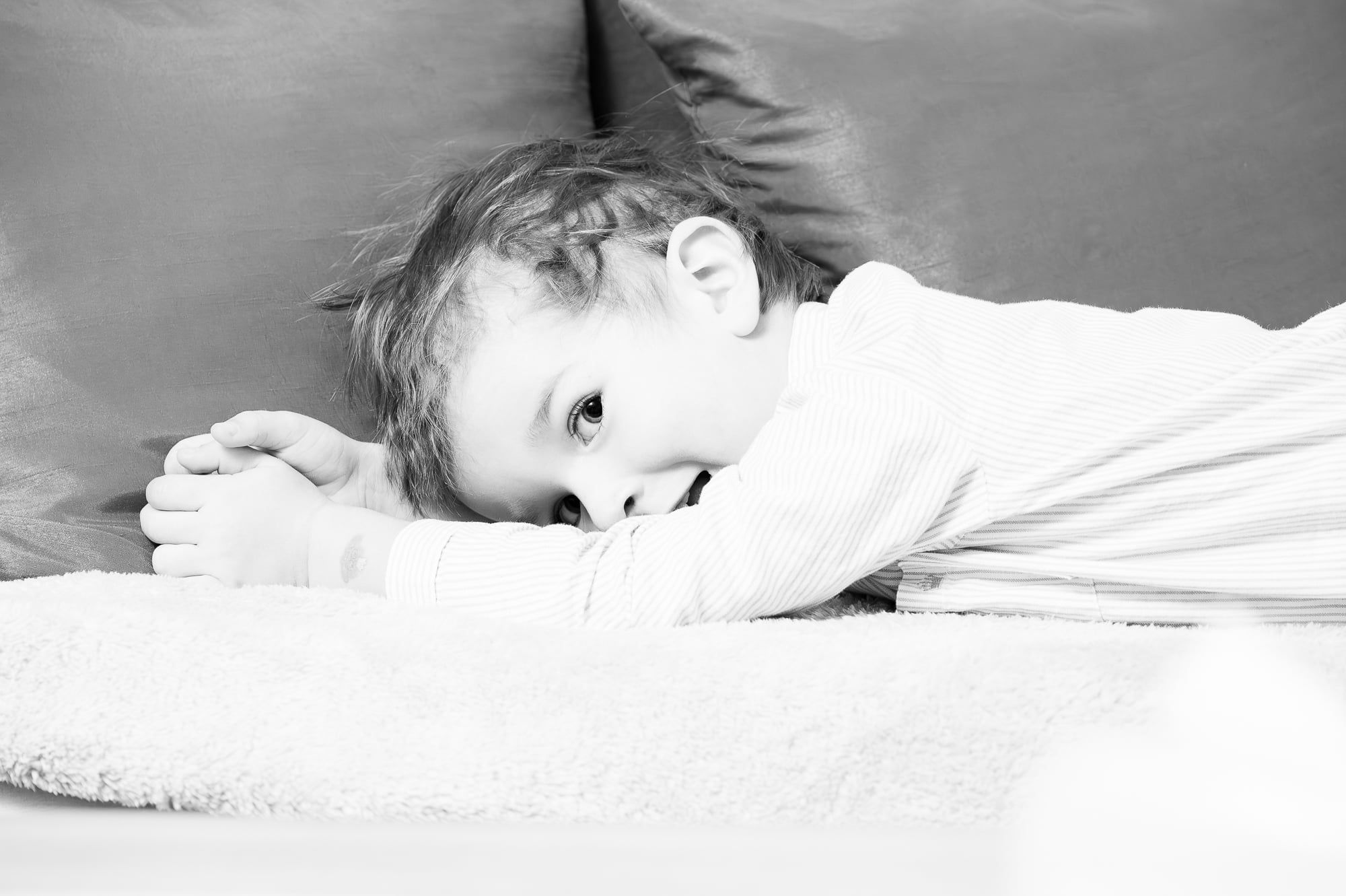 Kleinkind liegt auf einer Decke und schaut verschmitzt, Schwarzweiß – Familienshooting in Augsburg