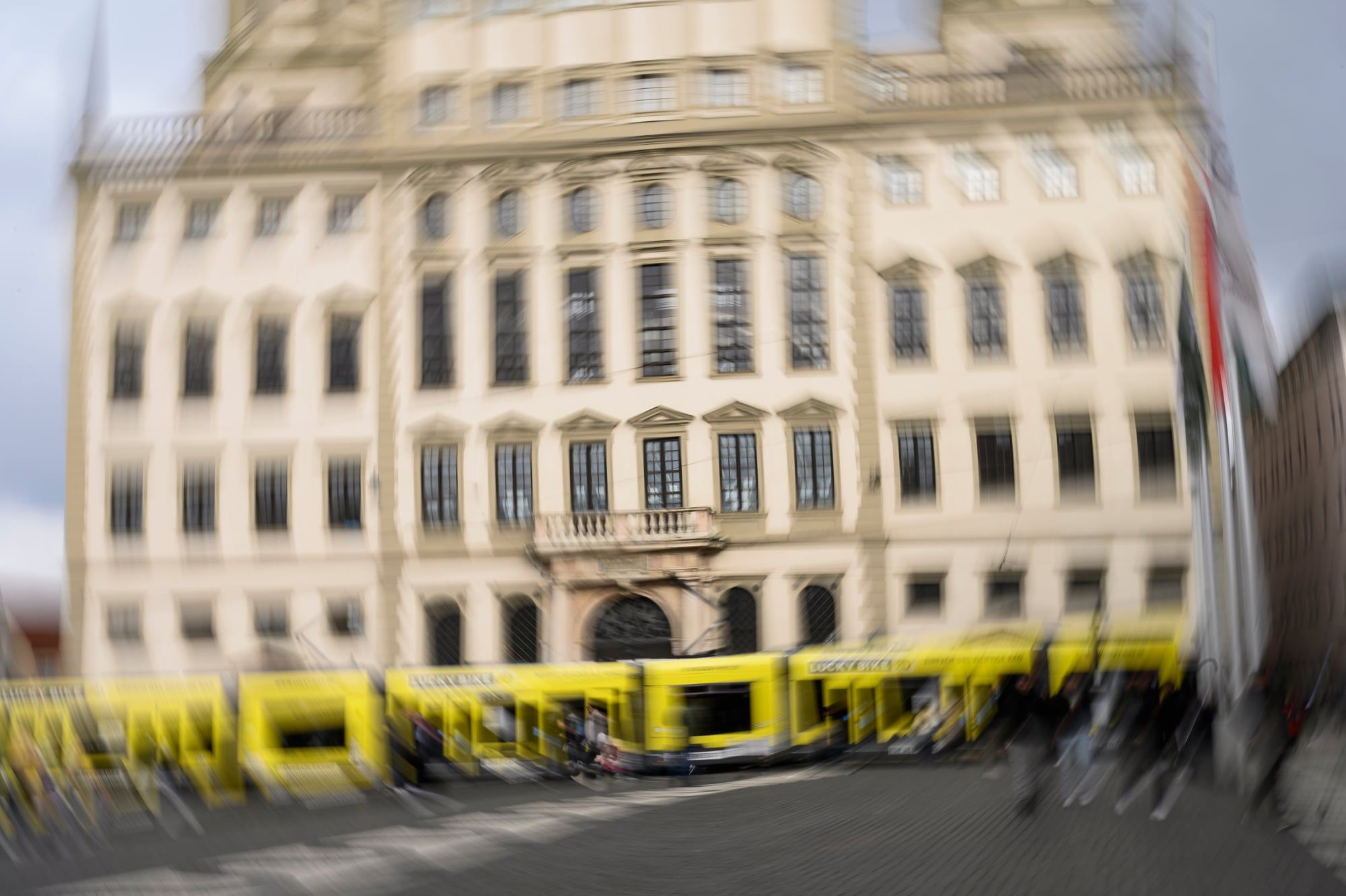 Verschwommene Mehrfachbelichtung des Augsburger Rathauses, davor eine gelbe Straßenbahn