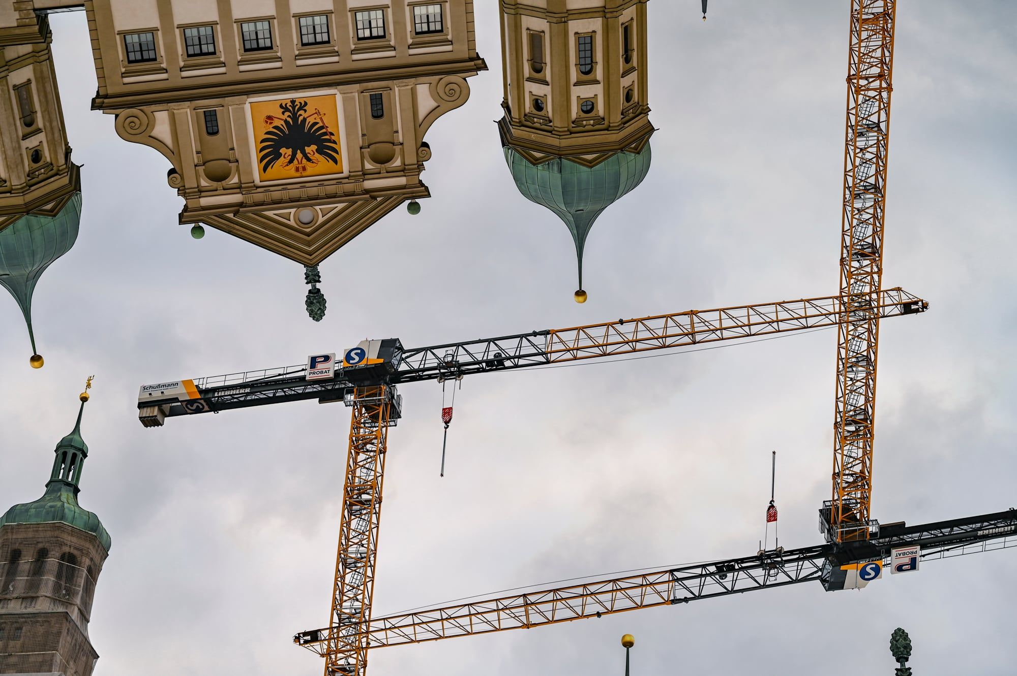 Mehrfachbelichtung: das Augsburger Rathaus kopfüber zwischen Baukränen am Himmel