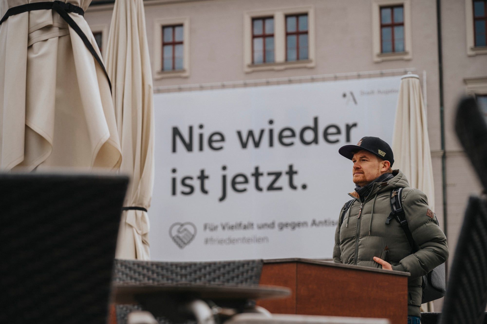 Mann mit Kappe vor dem Banner „Nie wieder ist jetzt“ am Augsburger Rathausplatz