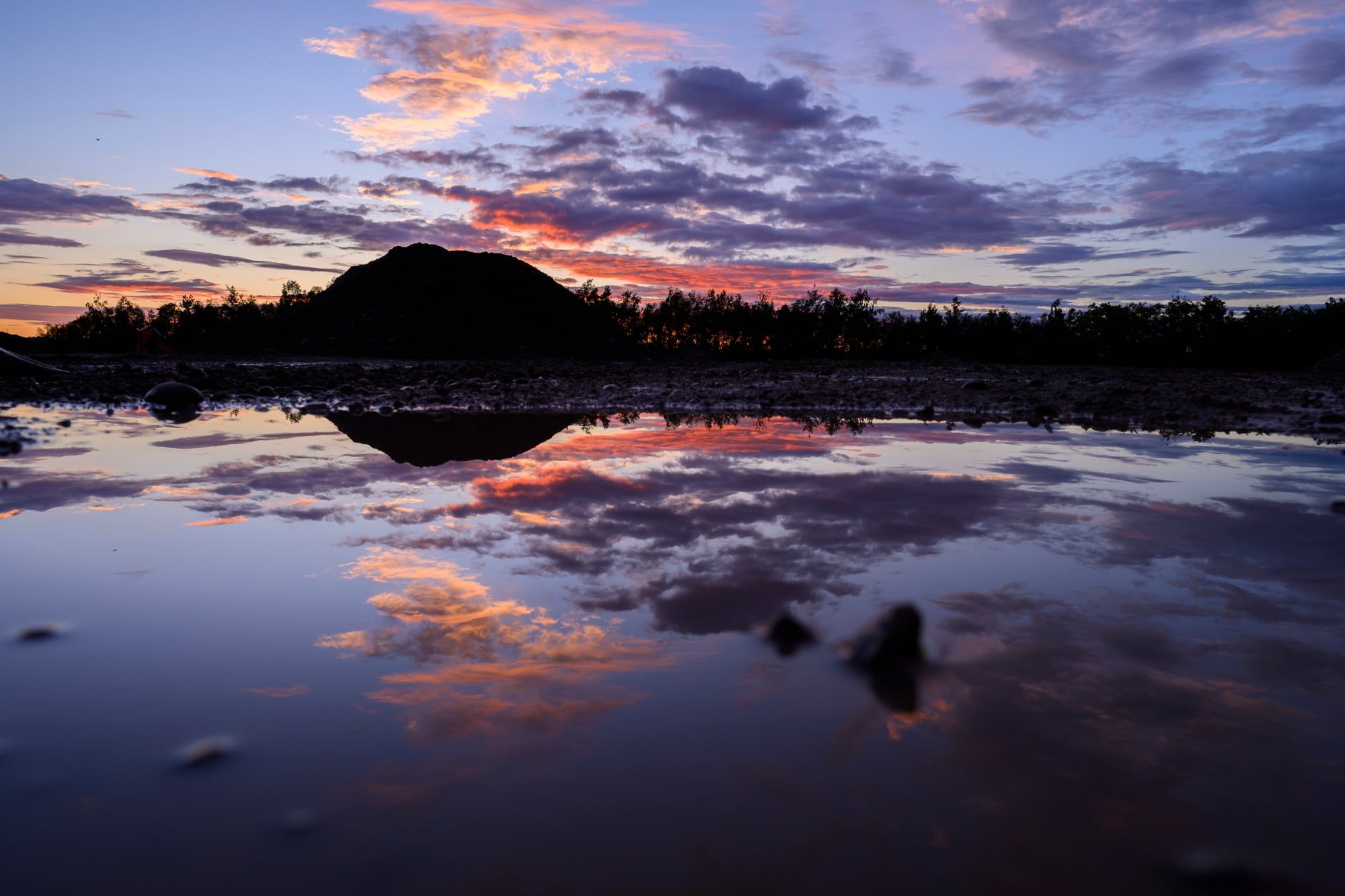 Ruhiger See spiegelt rosa und violett leuchtende Wolken nach Sonnenuntergang, aufgenommen in Bayern