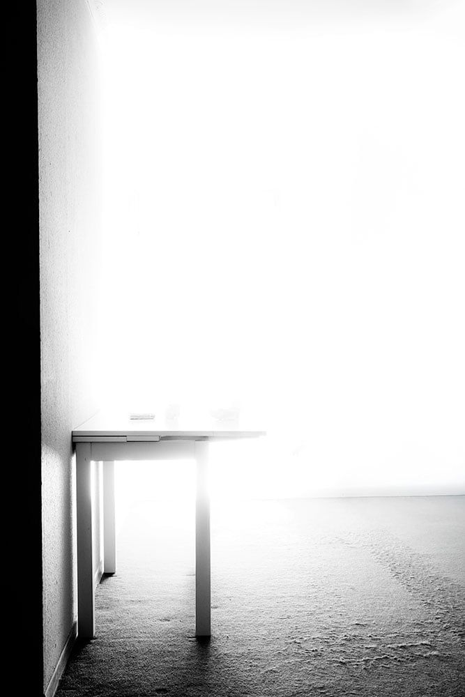 Stark aufgehelltes Bild des leeren Sets: Tisch vor weißem Hintergrund neben dem dunklen Türrahmen