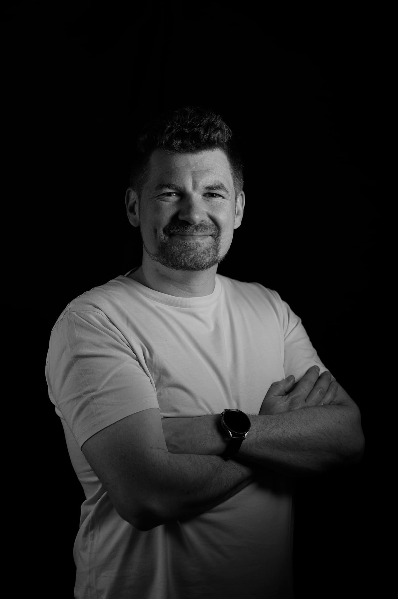 Daniel lächelt mit verschränkten Armen im Low-Key-Licht