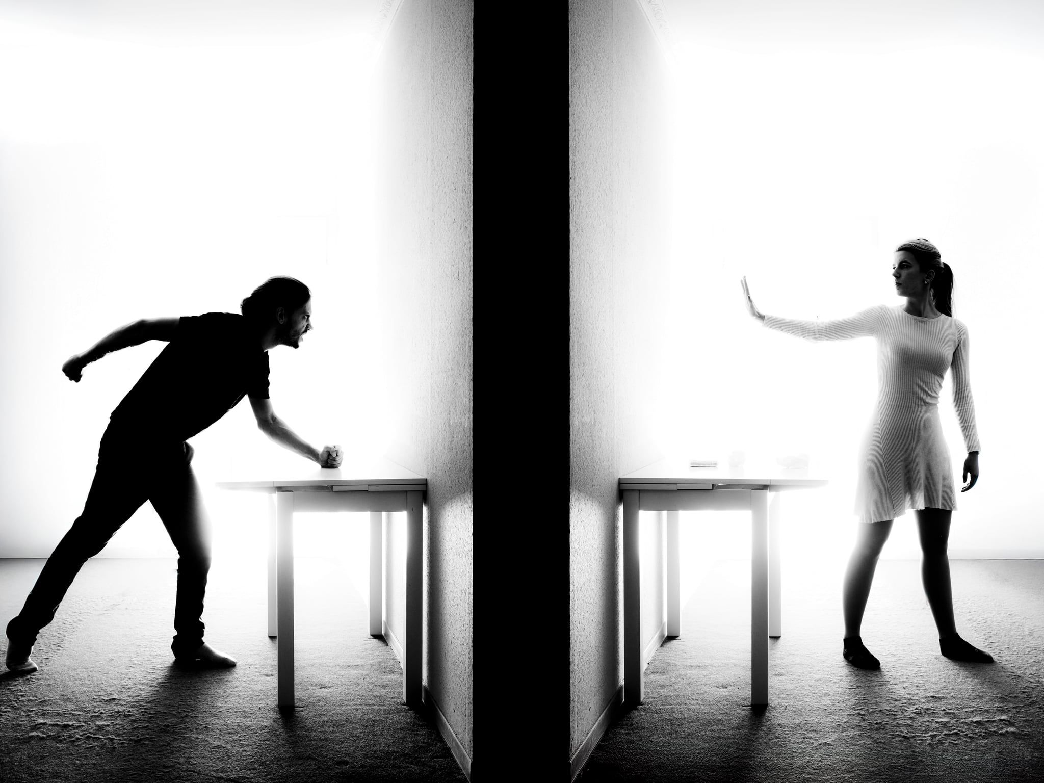 Komposition aus zwei Silhouetten an einer schwarzen Wand: links streckt sich ein Mann über den Tisch, rechts hebt eine Frau abwehrend die Hand