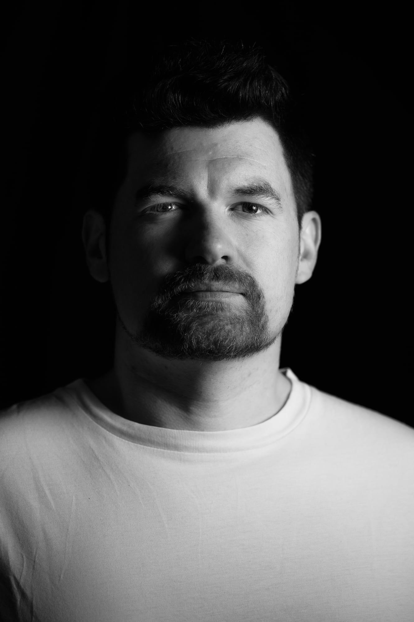 Schwarzweißes Low-Key-Portrait eines Mannes mit Bart im hellen T-Shirt – Portrait in München